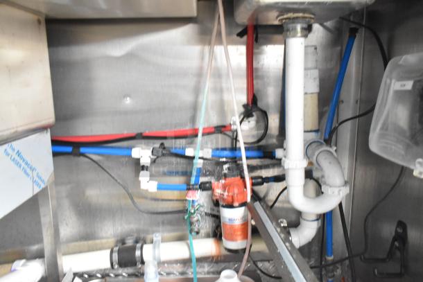 Plumbing system of Wendy's Mobile Kitchen Trailer, showing pipes, pump, and connectors in new, unused condition.