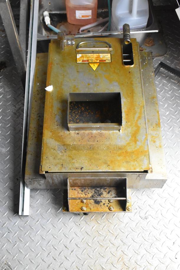 Rustic metal component inside Wendy's mobile kitchen trailer, featuring a stainless steel base and yellow caution label.