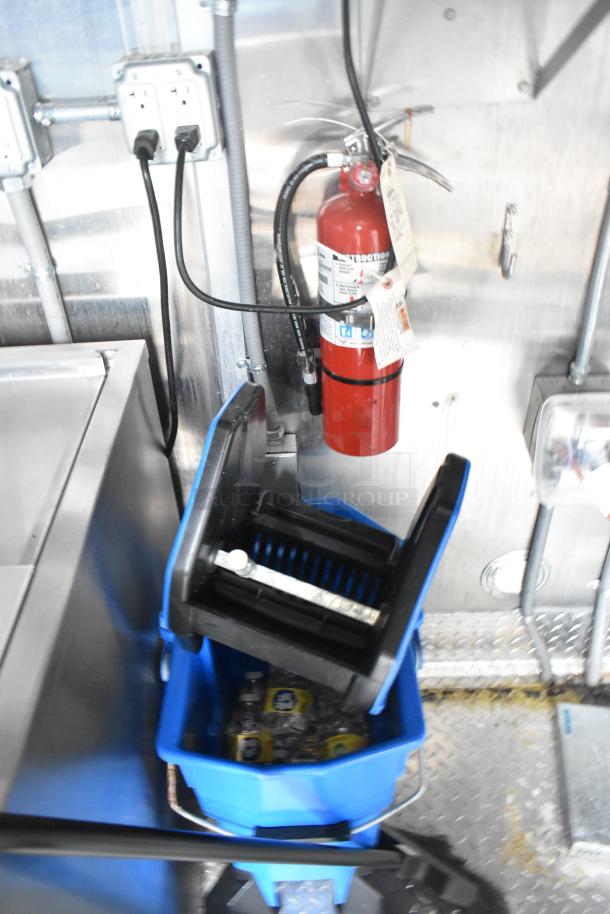 Wendy's mobile kitchen trailer interior featuring fire extinguisher, outlet, and cleaning supplies in a blue mop bucket.