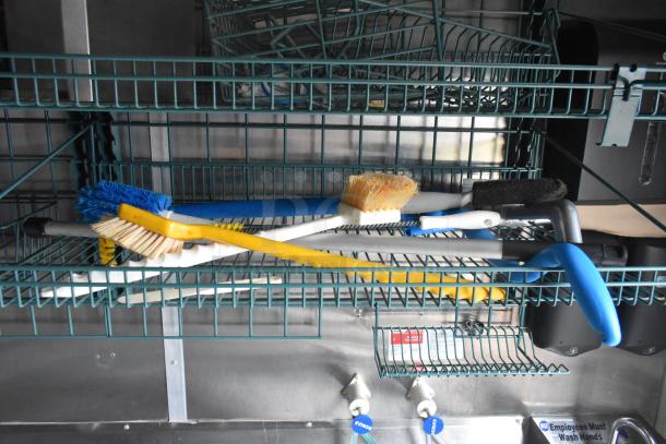 Interior of a Wendy's mobile kitchen trailer, showing various cleaning brushes on a wire rack, stainless steel sink below.