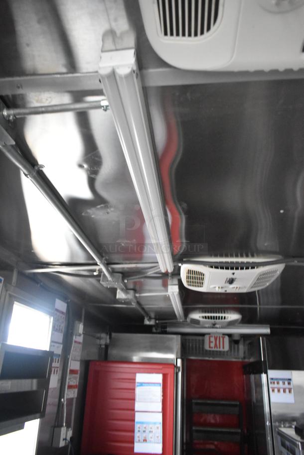 Interior of a brand new 8.5' x 28' mobile kitchen trailer, showcasing overhead piping and ventilation, pristine condition.