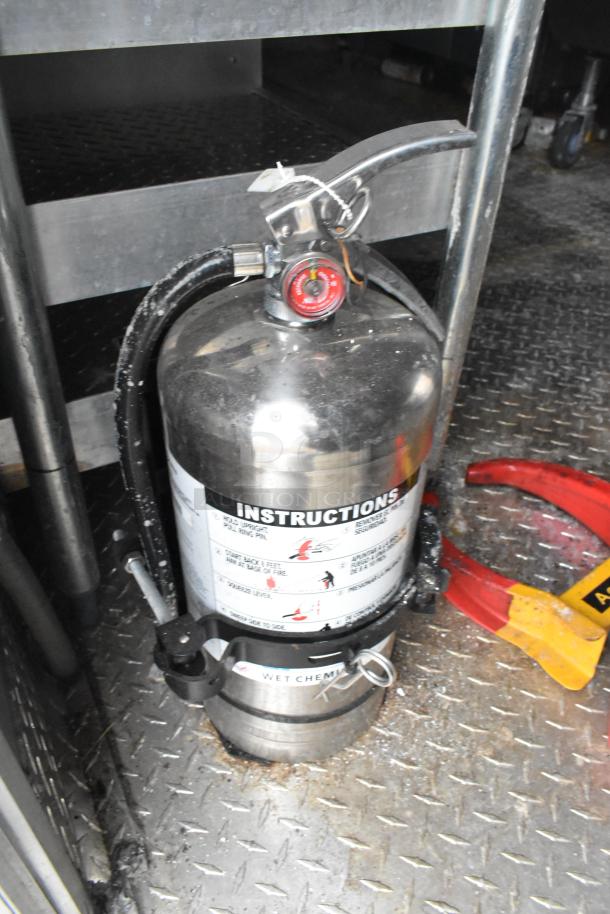 Fire extinguisher inside an unused mobile kitchen trailer, featuring instructions and a wet chemical label.
