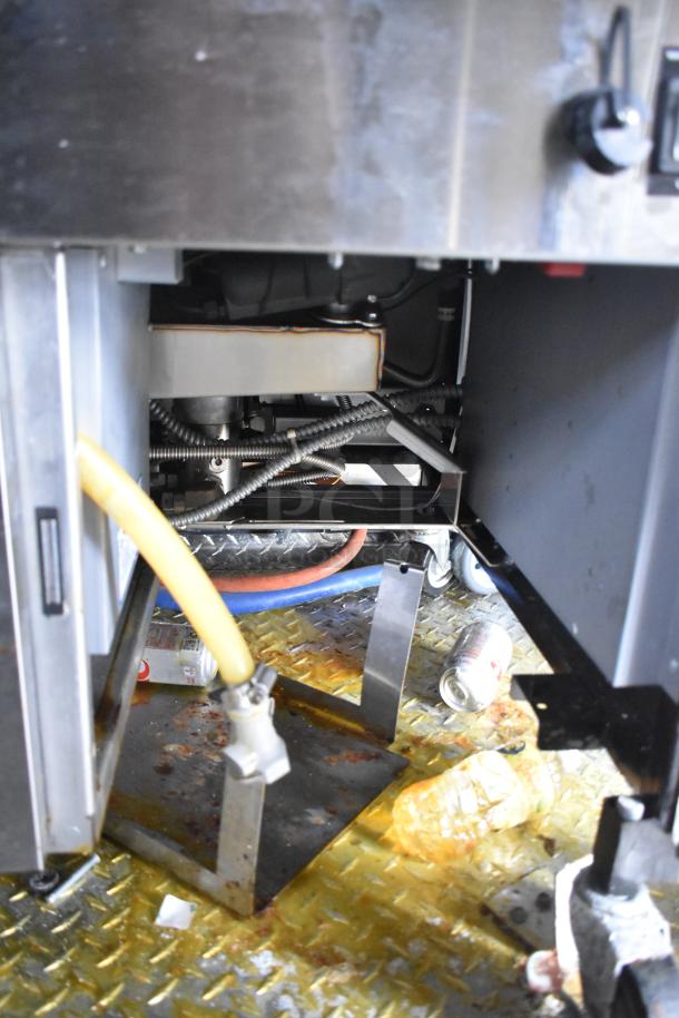 Interior view of a mobile kitchen trailer, showing plumbing, wiring, and floor area, with cans and bottles on metal grate.