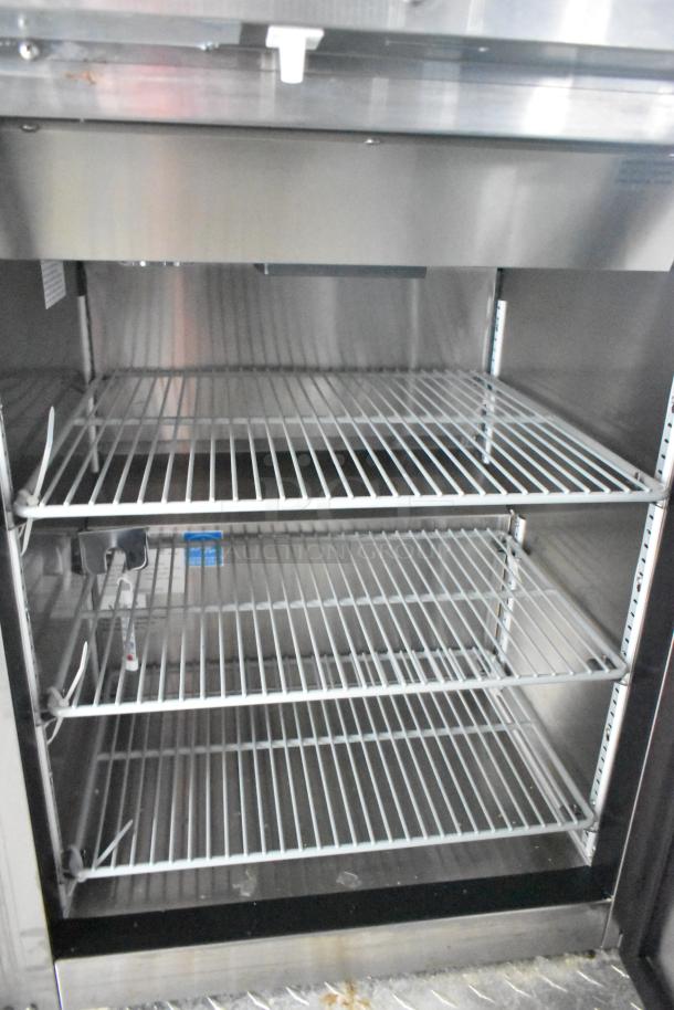 Interior view of a commercial refrigerator in a mobile kitchen trailer, showing three wire shelves and control panels.