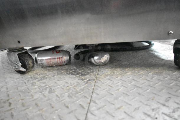 A close-up of a mobile kitchen trailer's metal interior floor with casters, soda can, and spoon visible.