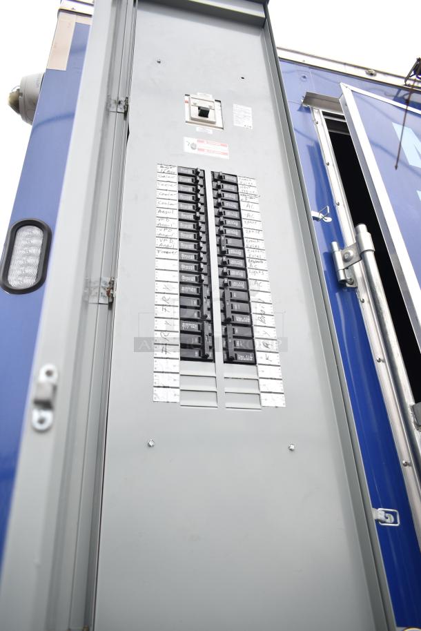 "2021 Rock Solid Cargo 28' fast food trailer's electrical panel, featuring labeled circuit breakers and clear casing."