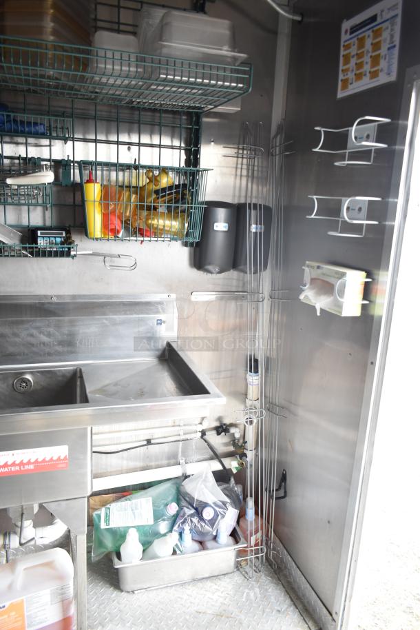Rock Solid Cargo fast food trailer interior showing metal sink, wire shelving with condiments and supplies, and storage area.