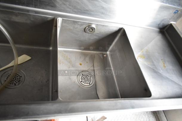 Stainless steel commercial sink in mobile kitchen trailer. Visible signs of use, including a crack and minor residue.
