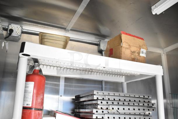 Interior of a 2021 Rock Solid Cargo 28' food trailer showing shelving with a fire extinguisher, storage box, and metal racks.