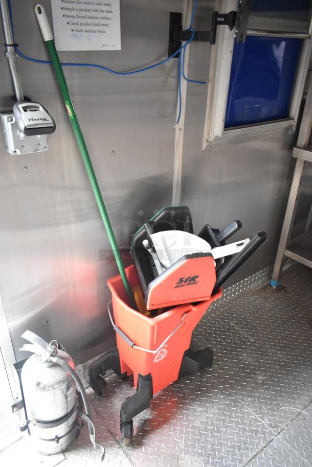 Mobile kitchen interior with mop bucket, mop, and fire extinguisher. Durable flooring and mounted appliances visible.