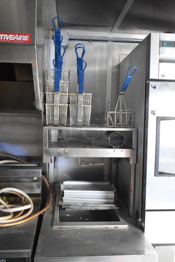 Commercial kitchen setup in a 2021 Rock Solid Cargo trailer featuring a CaptiveAire grease hood, fryer baskets, and refrigerator.