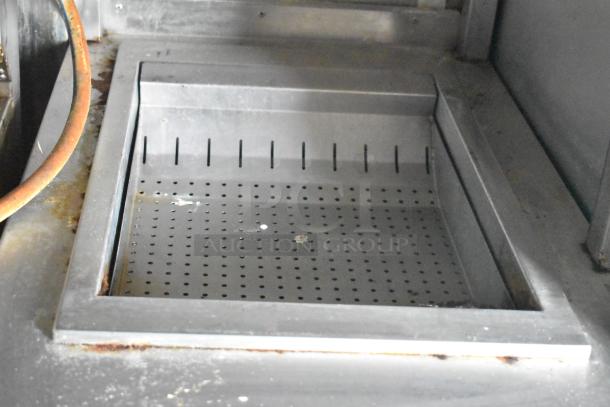 Metal holding bin inside a commercial kitchen trailer, showing slight wear. Perforated surface for food draining.