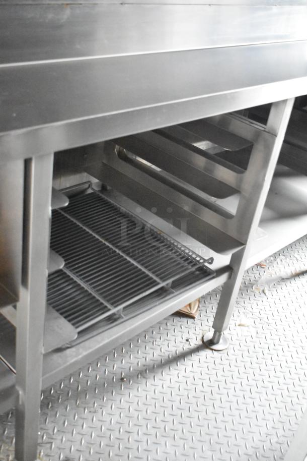 Stainless steel shelving unit inside a mobile kitchen, featuring a grated bottom shelf and diamond plate flooring.