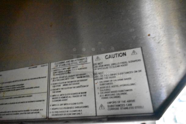 Close-up of caution and cleaning instructions on a stainless steel hood. Text advises against using harsh cleaners.