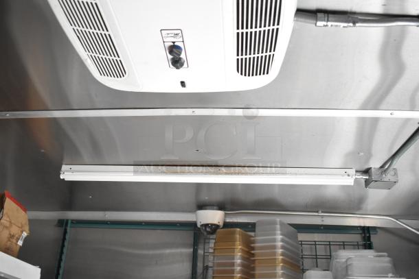Interior ceiling view of a 2021 Rock Solid Cargo 28' Fast Food Trailer. Visible are an air vent, fluorescent light, security camera, and stacked trays.