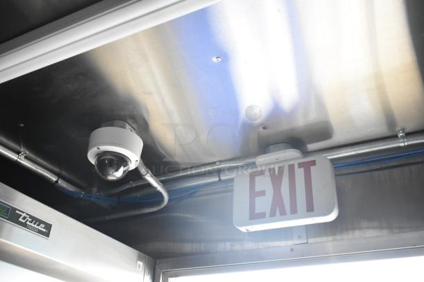 Exit sign and security camera inside 2021 Rock Solid Cargo 28' mobile kitchen trailer, featuring a True freezer tag.