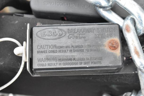 ESCO breakaway switch on trailer, 12V DC, warning labels for brake and plunger removal, attached chain visible.