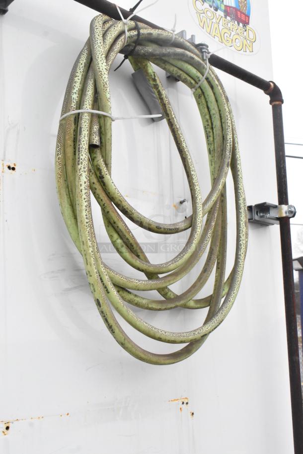 Green hose hanging on the side of an ATX trailer with "Covered Wagon" decal. Visible rust and wear on the surface.