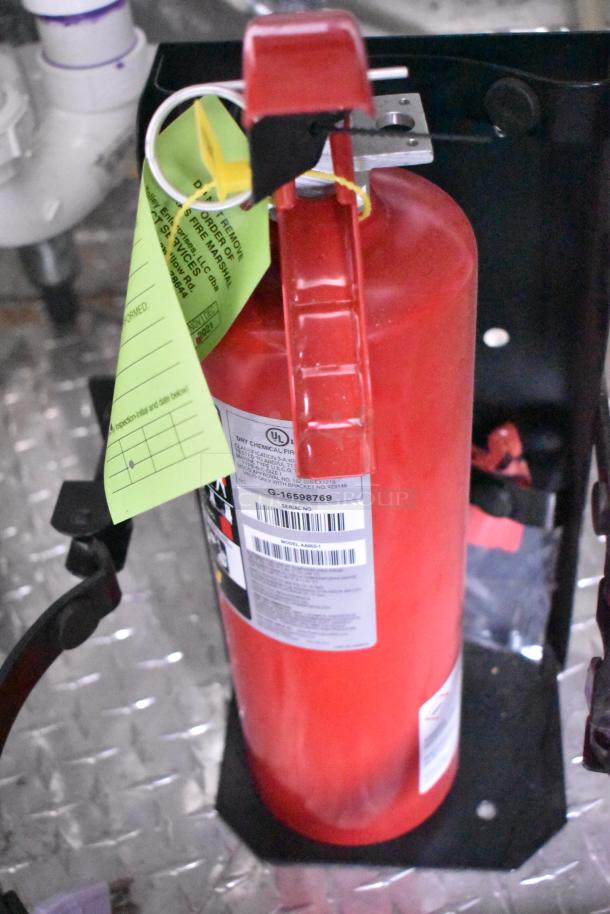 Red fire extinguisher mounted in a trailer with inspection tag visible. Includes UL label and model information.