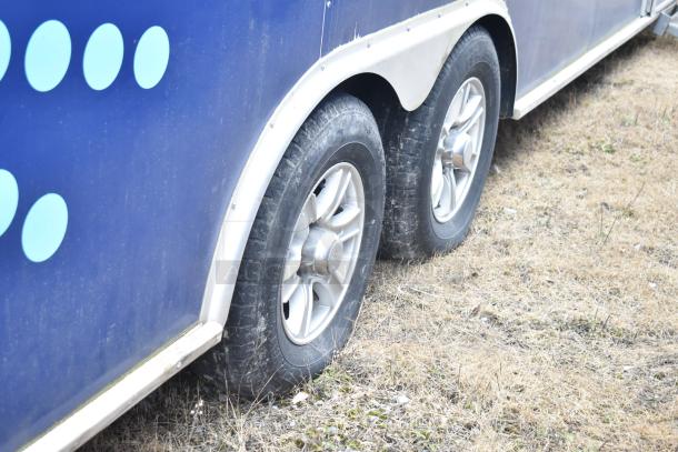 2019 Cruising Kitchens trailer wheels, dual axle, blue exterior, on grass. Includes grease hood, fire suppression, Arctic Air units.