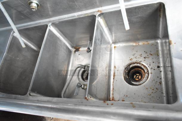 Stainless steel sink with three compartments, showing signs of use and rust around drains. Part of a Cruising Kitchens trailer.