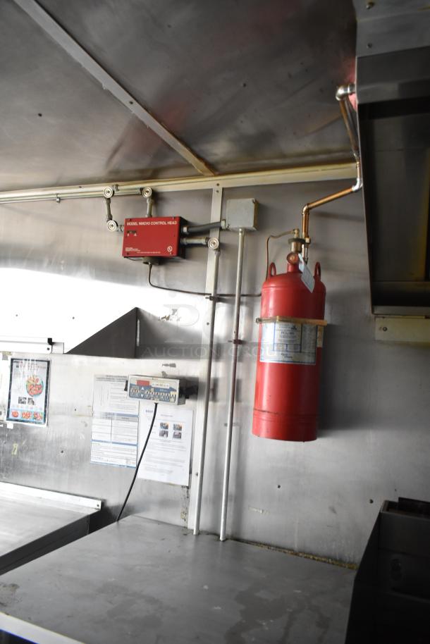 Interior of a 2019 Cruising Kitchens trailer featuring a red fire suppression system and metal surfaces, with visible safety labels.