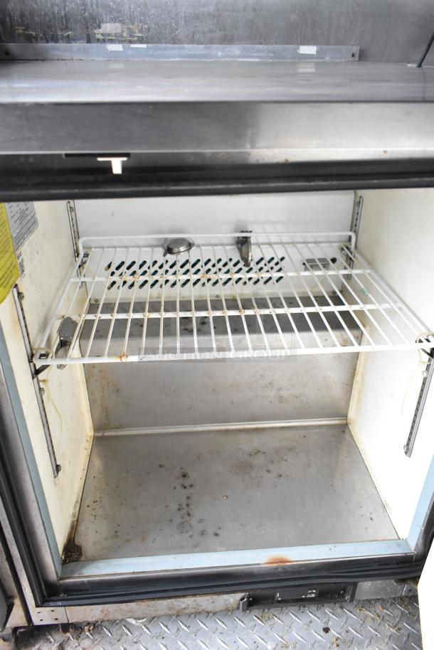 2019 Cruising Kitchens trailer interior showing an Arctic Air cooler with shelving, minor wear, and diamond plate flooring.