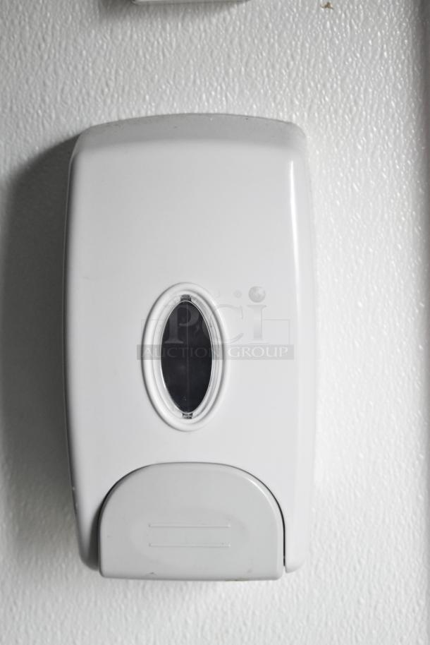White wall-mounted dispenser for soap or sanitizer, featuring an oval window for content level visibility.
