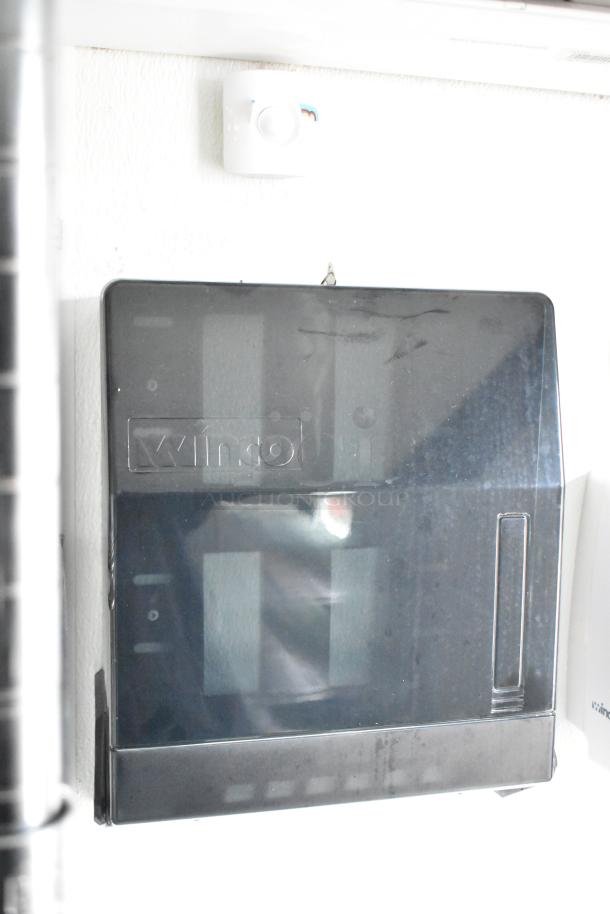 Black Winco paper towel dispenser mounted on a white wall.