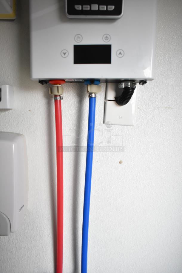Close-up of a wall-mounted device with control buttons, red and blue hoses attached for plumbing connections.