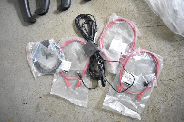 Assorted black and red cables with Ethernet connectors, packaged in clear plastic bags, on a concrete floor.