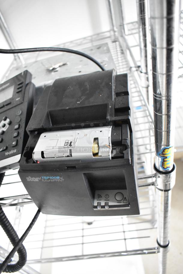 Star TSP100III futurePRNT receipt printer, black, mounted on wire shelving unit. Visible power buttons and connectivity icons.