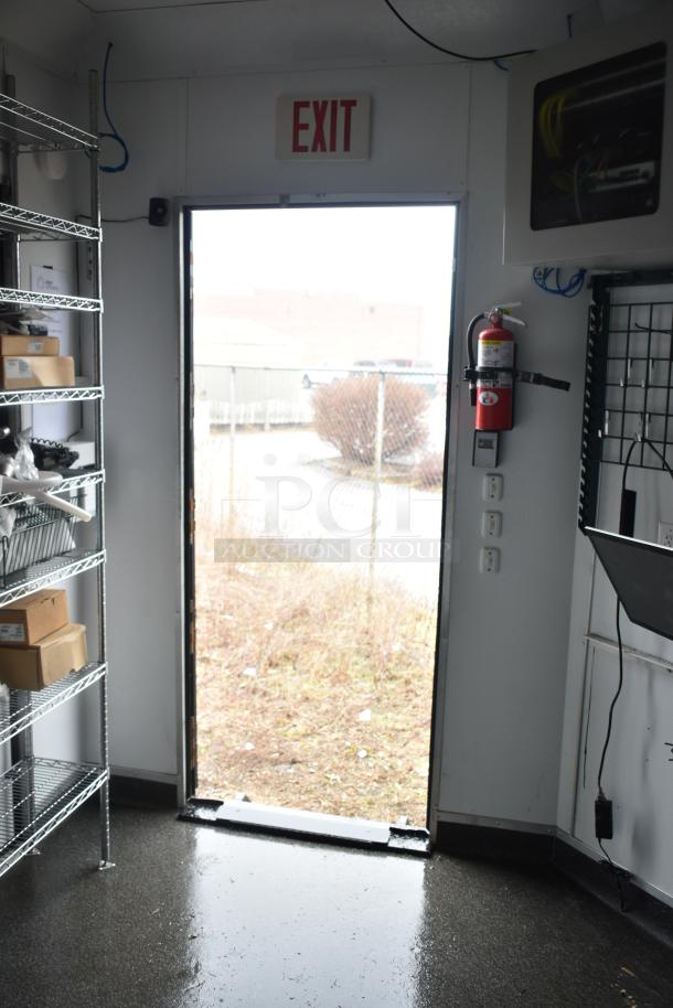 Inside of 2020 SDG 8.5' x 20' food trailer shell, featuring wire shelving, exit sign, fire extinguisher, and IT/network cabinet.