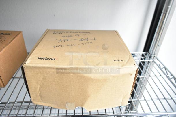 Cardboard box labeled "Verizon" and "Yealink" on a metal shelf; handwritten notes and phone number visible on top.