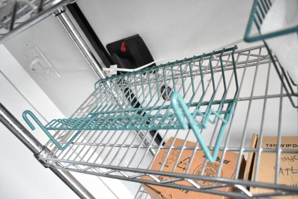 Metal wire shelving in SDG 8.5' x 20' food trailer shell, featuring teal racks. Boxes sit below. Ready to customize.