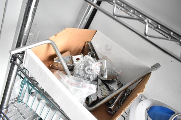 Box of metal brackets and screws on a wire shelving unit inside a 2020 SDG 8.5' x 20' food trailer shell.