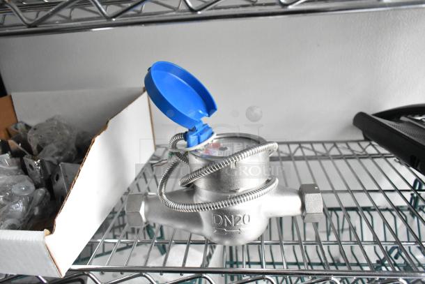 Stainless steel DN20 water meter with blue plastic cover on wire shelving.