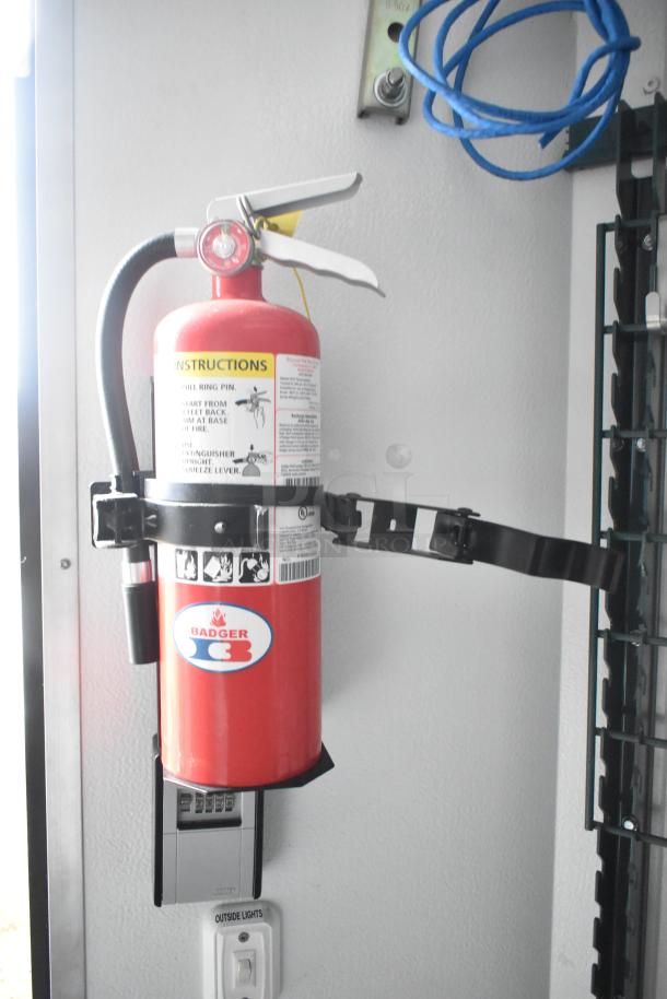 Red fire extinguisher mounted inside SDG food trailer, featuring Badger branding and safety instructions.