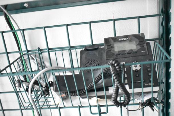 A telephone with a cord and wires stored in a green wire shelving unit, part of a 2020 SDG food trailer shell.