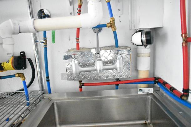 2020 SDG 8.5' x 20' food trailer sink area, featuring a dual-handle faucet, plumbing pipes, and wire shelving; ready for customization.