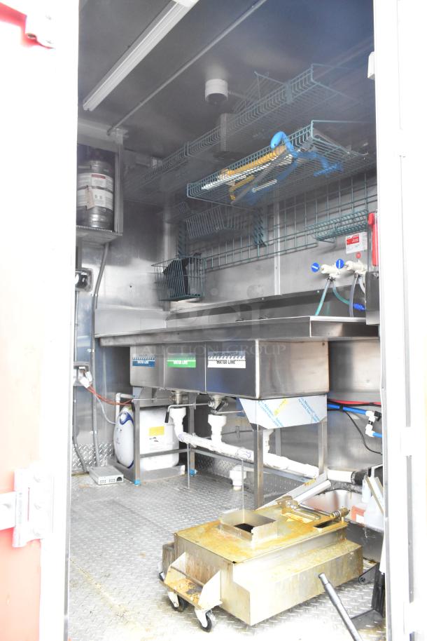 2021 Titanium Cargo 8.5' x 28' mobile kitchen trailer interior; features sinks, stainless steel fittings, storage racks, and plumbing.