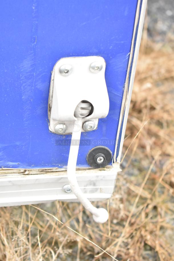 Blue mobile kitchen trailer hitch detail, showing metal latch and white handle on rust-marked panel.