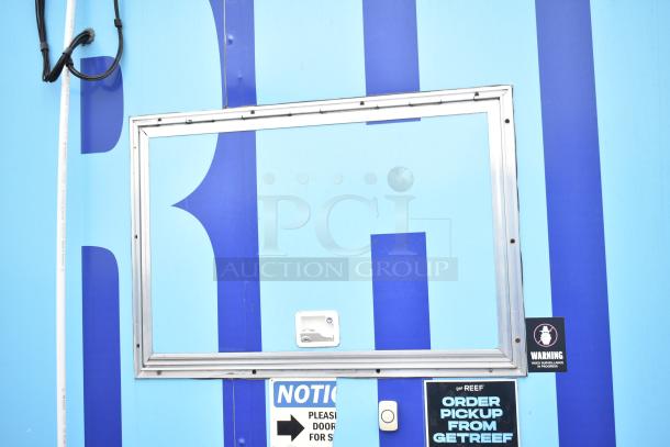 Mobile kitchen trailer with blue exterior featuring service window, surveillance warning, and signage for order pickup.