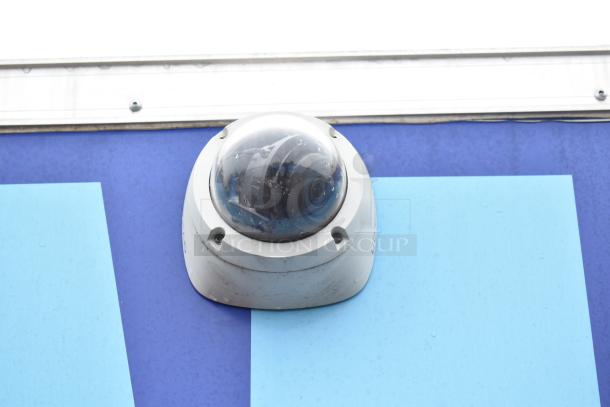 An outdoor security camera mounted on a blue wall.