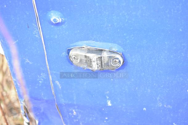 Blue mobile kitchen trailer surface with a scratched exterior. Visible mounted light with clear plastic cover and screws.