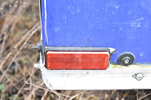 Blue mobile kitchen trailer corner with a red reflector and visible wear. No kitchen equipment shown in this image.
