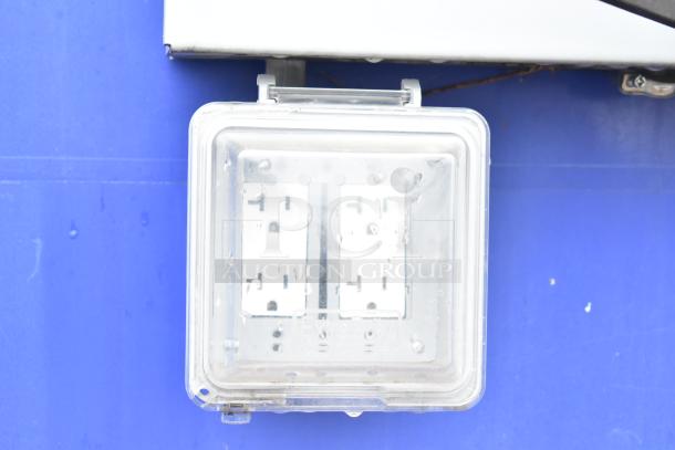 Weatherproof electrical outlet on blue wall, featuring a clear protective cover labeled "Extra Duty." Visible double outlets inside.