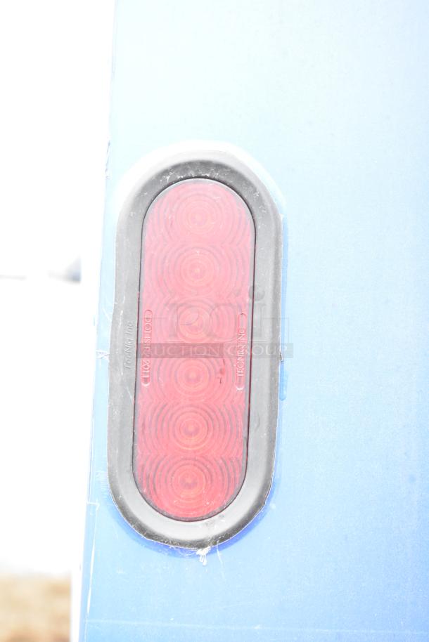 Red oval trailer light on a blue mobile kitchen trailer. DOT/SAE markings visible on the lens.