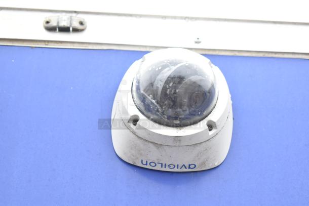 Security camera mounted on a purple surface, slight signs of wear, with branding text that appears inverted.