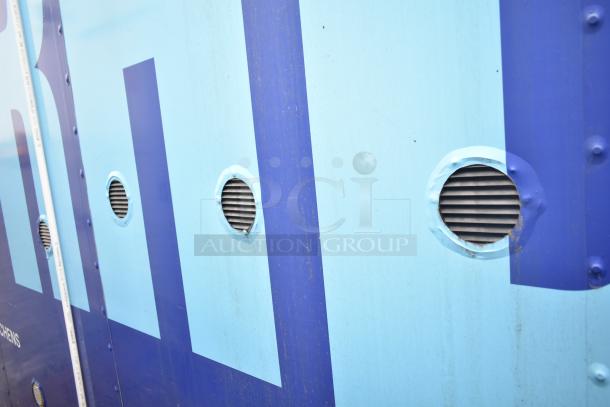 Exterior of a mobile kitchen trailer, featuring vents and a blue design, housing CaptiveAire hood, Pitco fryers, Arctic Air equipment.